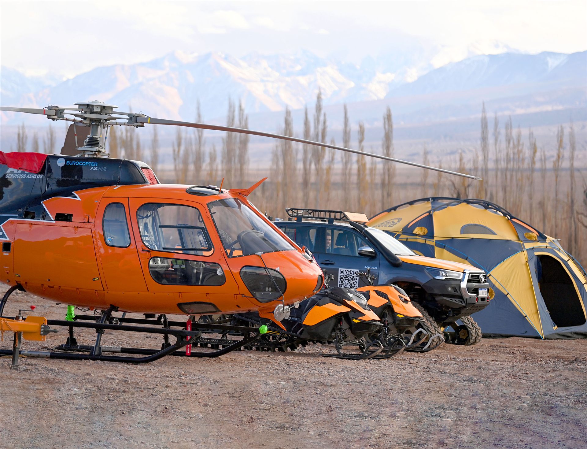 Helicóptero, motos de nieve y camioneta del equipamiento GHM frente a la cordillera