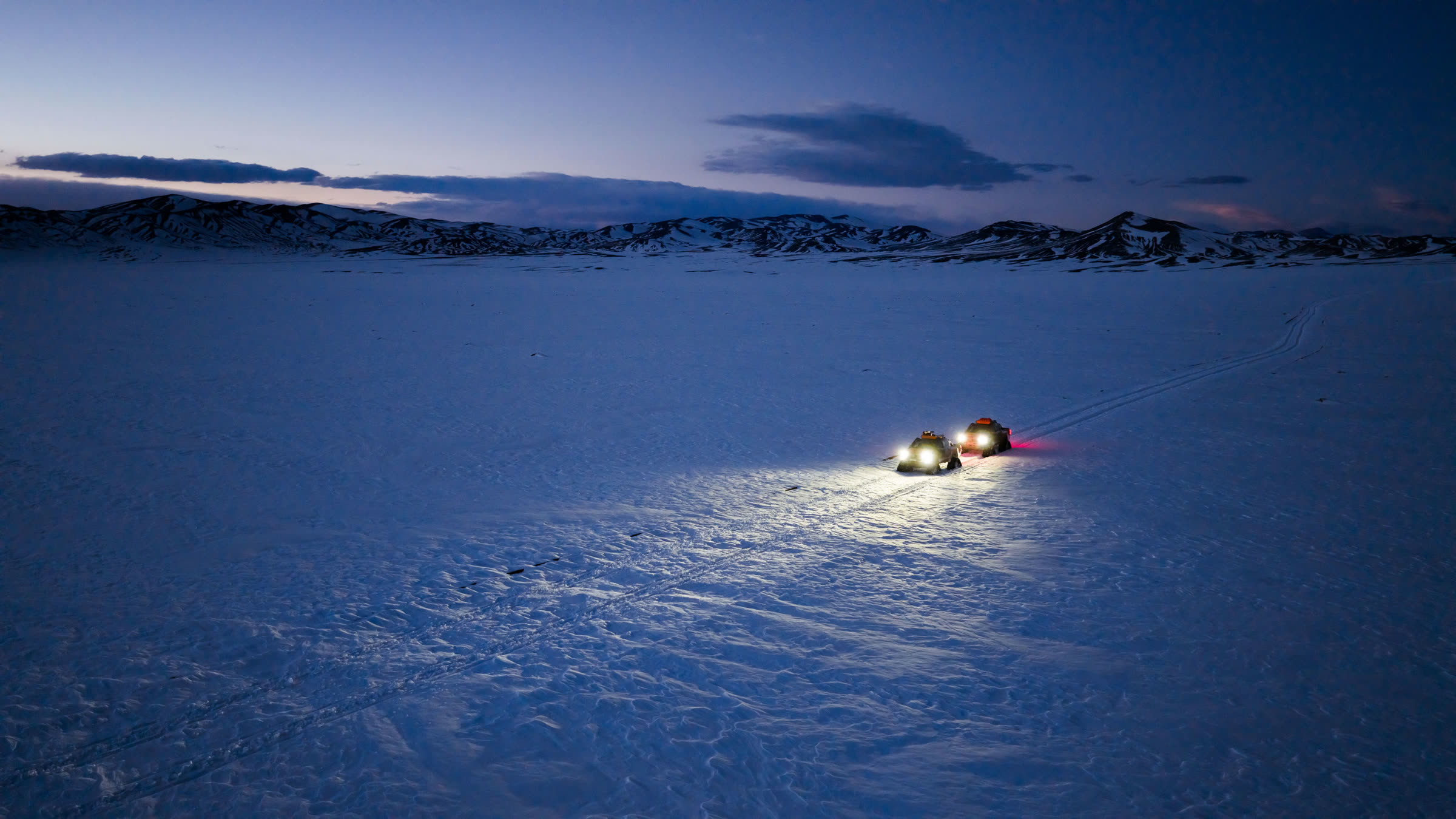 Vehículos de GHM avanzando al anochecer sobre la nieve en alta montaña